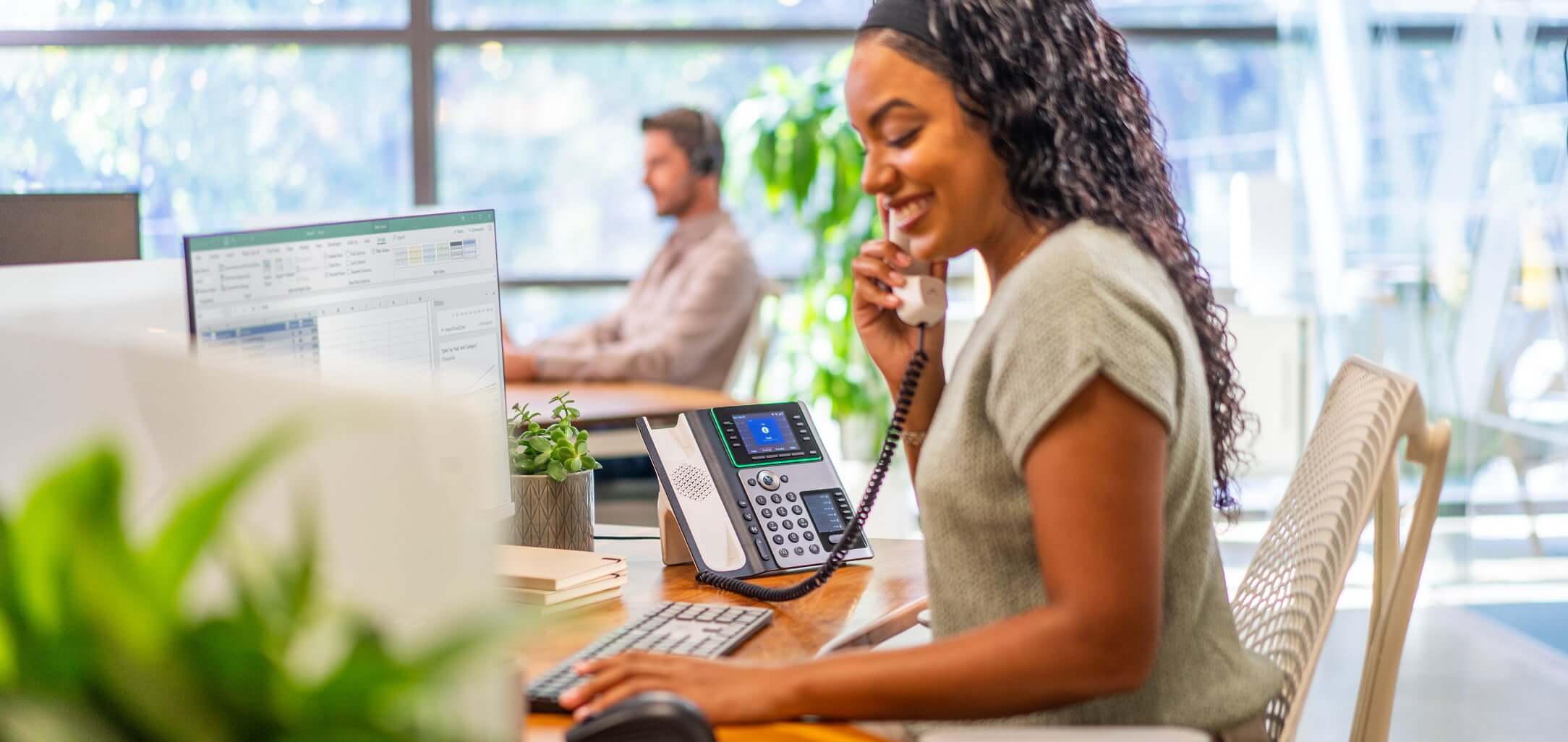 Woman seated at desk in open office using Poly Edge E450 desk phone