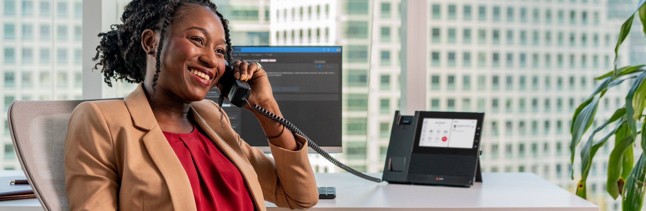 Smiling woman seated at office desk  using Poly CCX desk phone with handset during a zoom call​