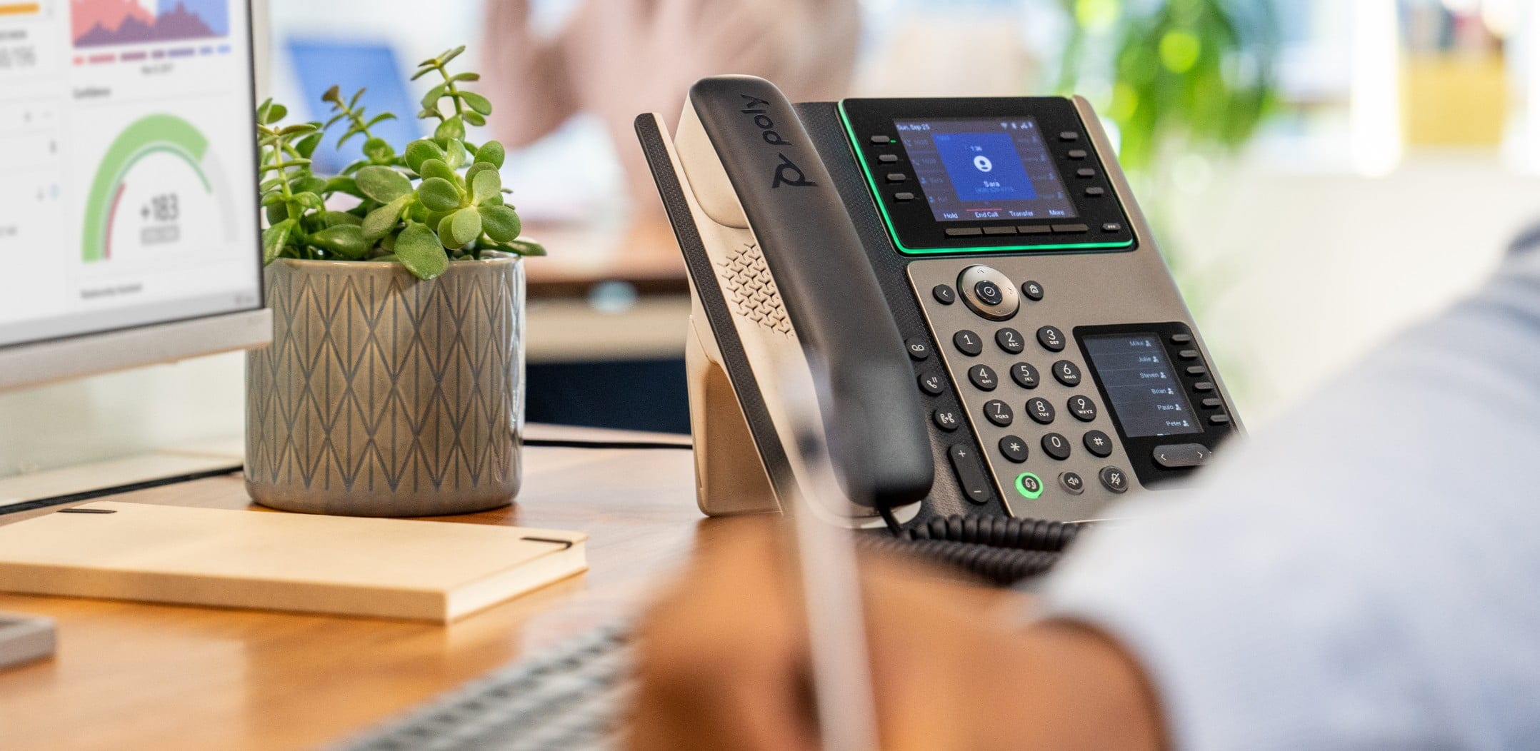 Man at office desk, writing notes while using Poly Edge E450 IP desk phone ​