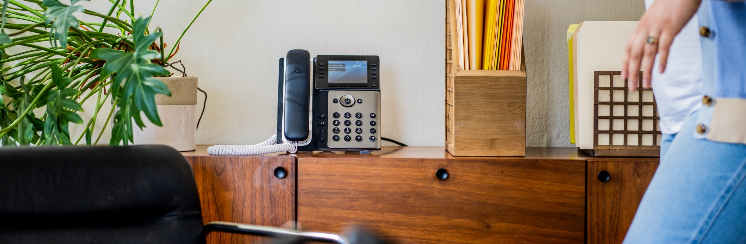 Poly Edge E350 desk phone with handset, located on credenza behind home office desk​