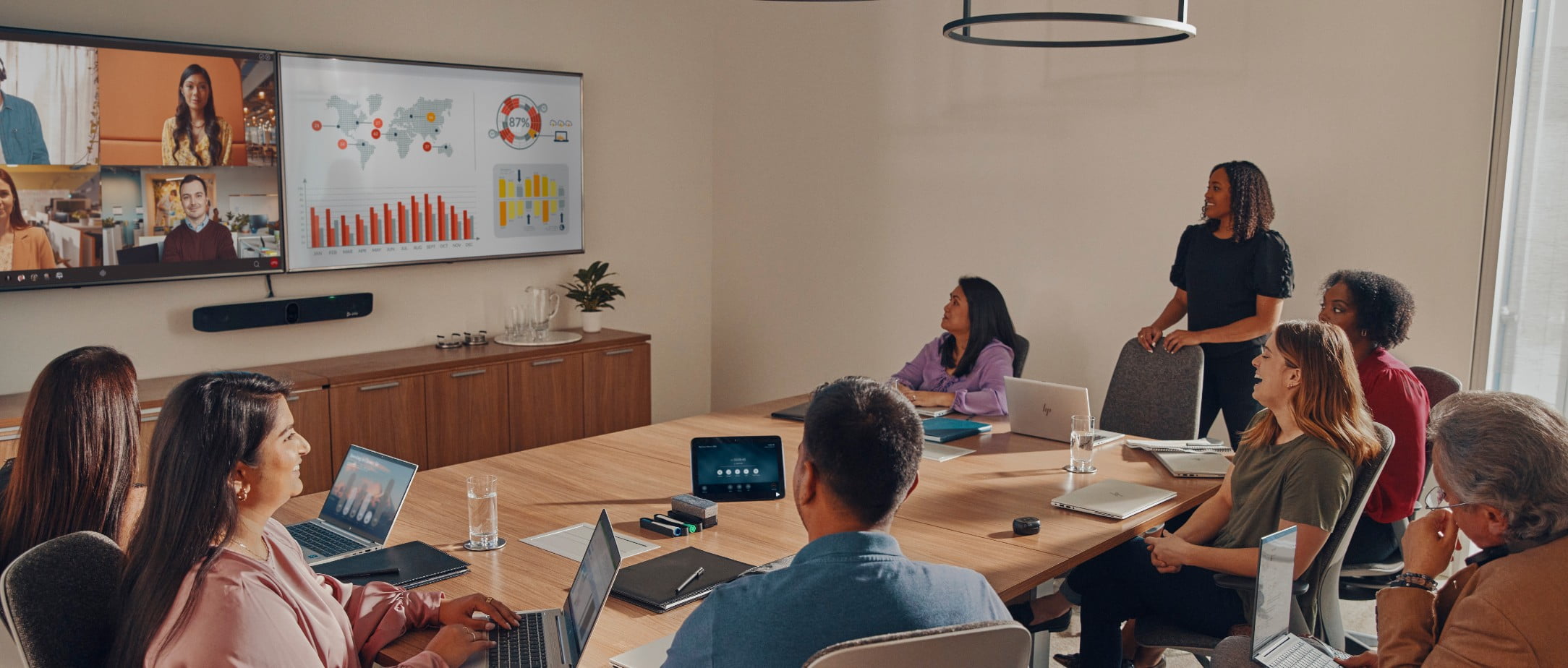 Das Poly Studio X70 Videokonferenzsystem und Laptops von HP werden von einer großen Gruppe im Konferenzraum bei einem Videocall mit Remote-Teams eingesetzt