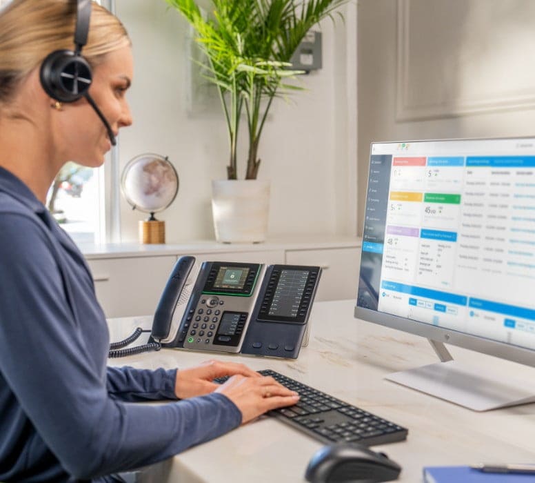 Woman at desk looking at onscreen content while using Poly headset with Poly E450 desk phone for a call