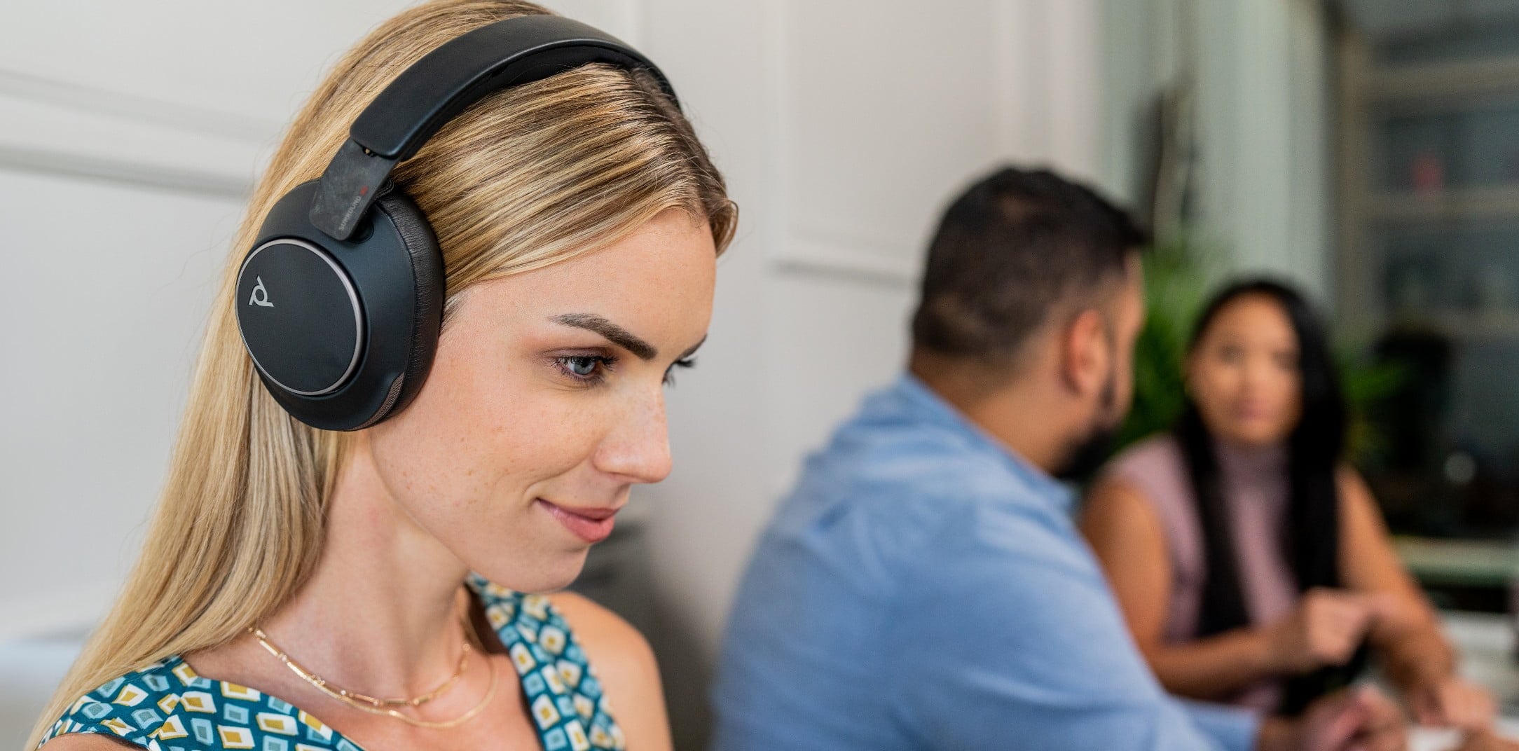 Mujer en una oficina usando auriculares Poly Voyager Surround 80 con cancelación de ruido