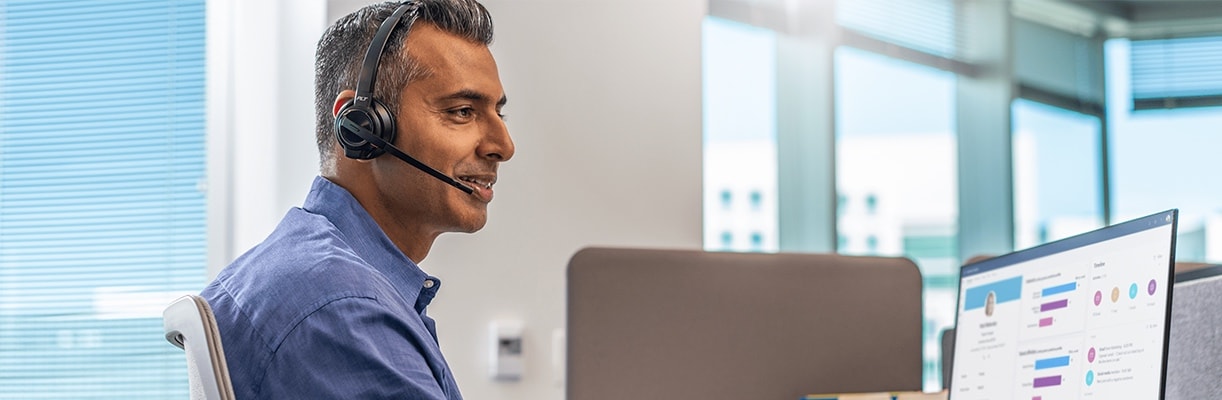 A man using the Poly Savi 8400 Office Series headset, while working on his computer