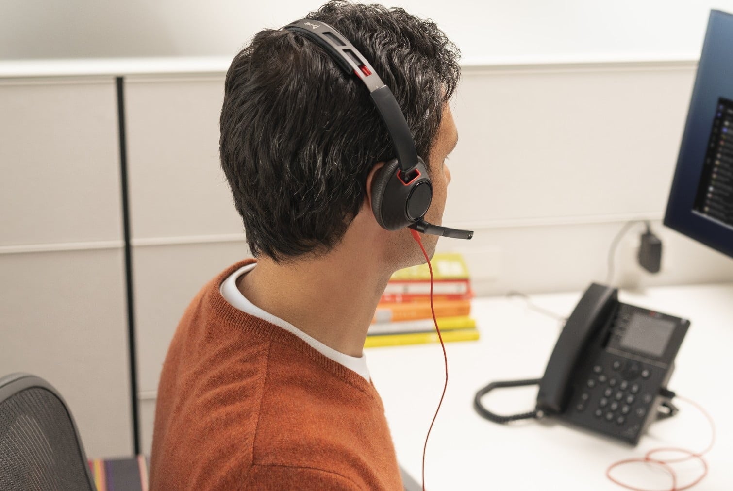 Man seated in office cubicle desk wearing Poly Blackwire 5200 USB wired headset connected to desk phone