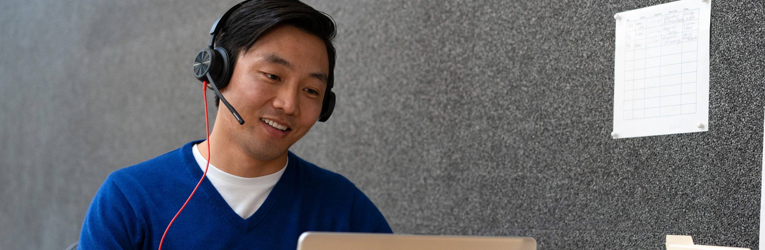 Man seated at office desk using laptop and wearing Poly Blackwire 8225 USB wired headset