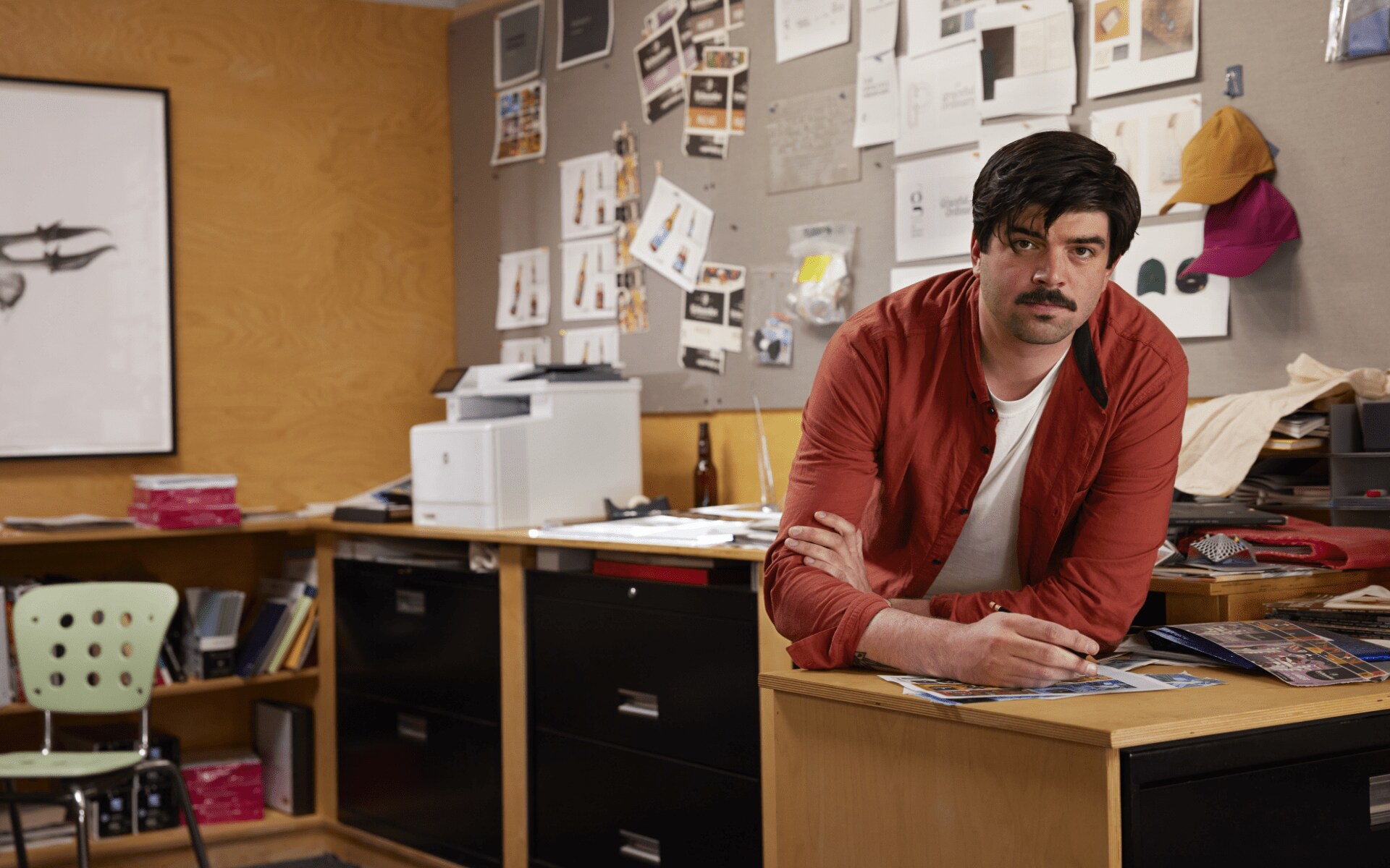 Man in small office looking at color documents with HP laserjet printer behind him