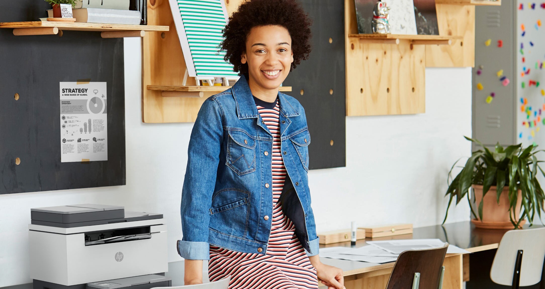 A smiling woman in the office, leaning on a desk with an HP Laserjet Pro printer on it