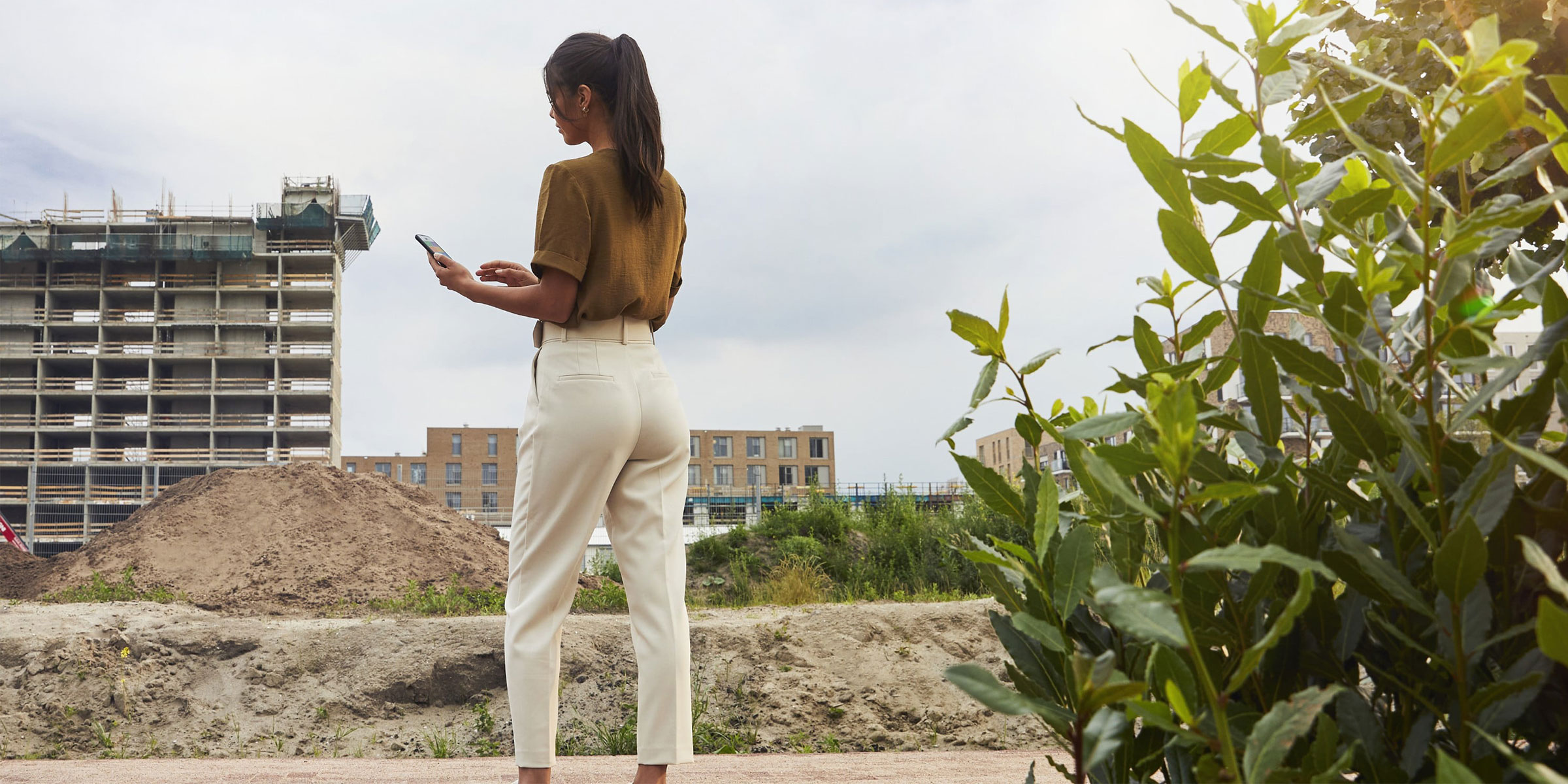 Personne consultant un appareil mobile devant un chantier de construction en extérieur