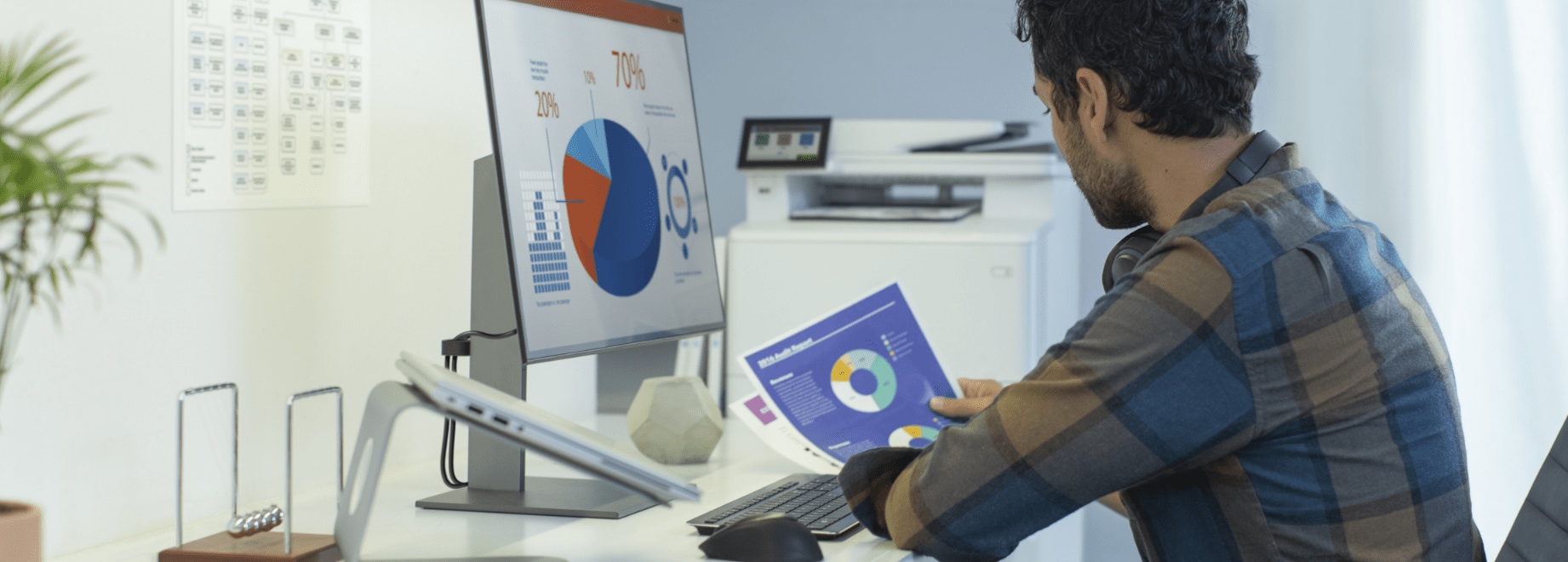 Man at workstation comparing color printed document with image on HP monitor and HP LaserJet Enterprise printer behind him