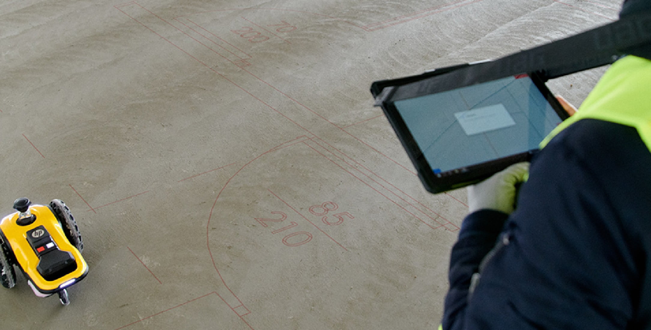 A construction worker with a tablet in front of a HP SitePrint layout robot.