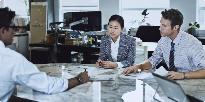 A man showing some printed data to his 2 co-workers in a rounded table.