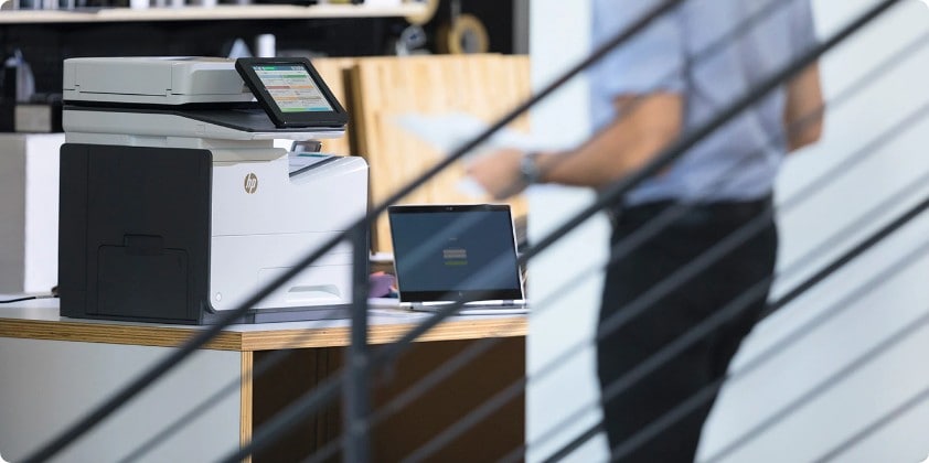 An HP printer aside of an HP laptop in top of a wooden desk.