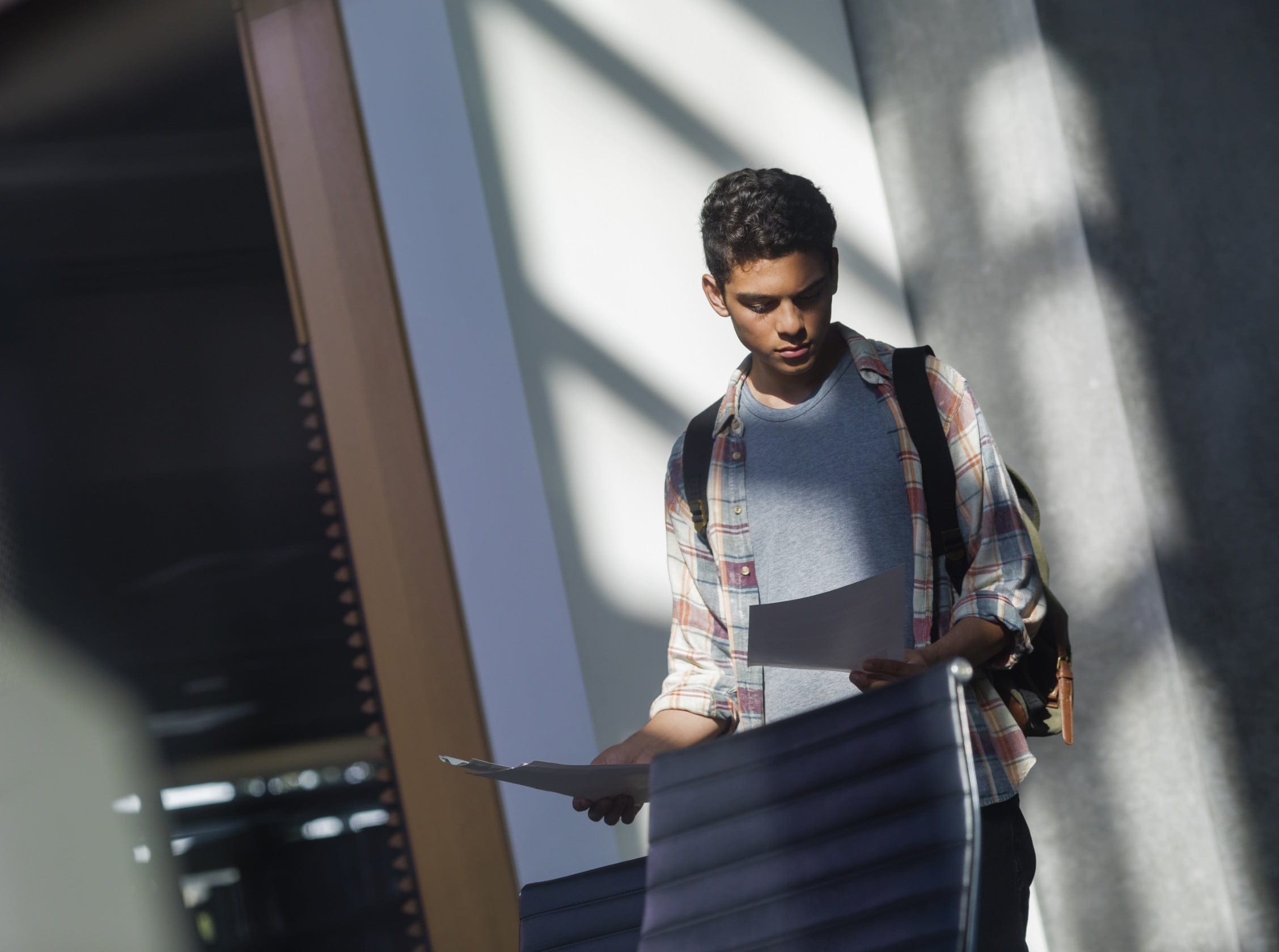 Teenaged student with backpack looking at printed worksheets