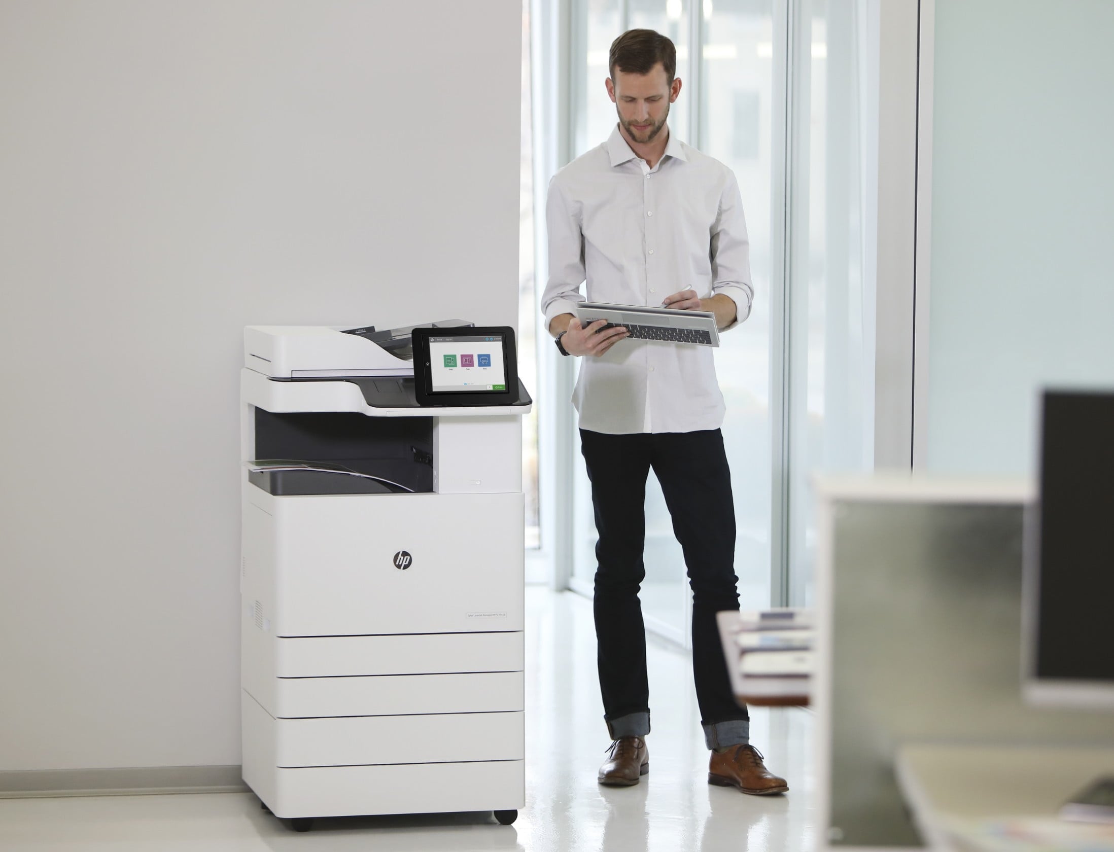 Mitarbeiter steht vor einem HP LaserJet Enterprise Drucker und sieht sich Ausdrucke an