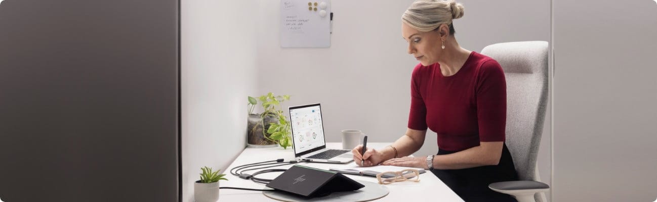 A woman working at her office using an HP laptop connected to an HP Presence Room Assistant device.