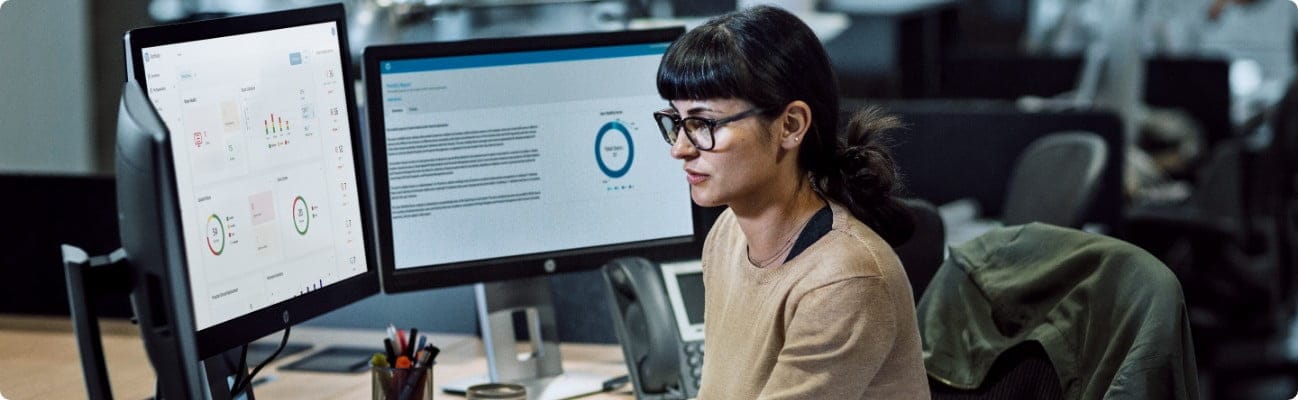 A woman checking some data on her 3 HP monitors connected to and HP computer on top of her office desk.