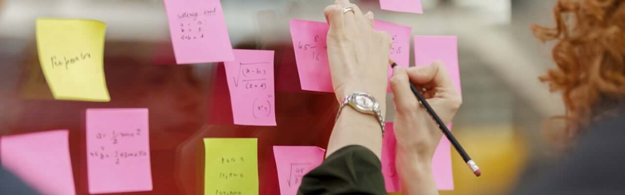 Woman writing some numbers on one of several sticky notes on a glass window