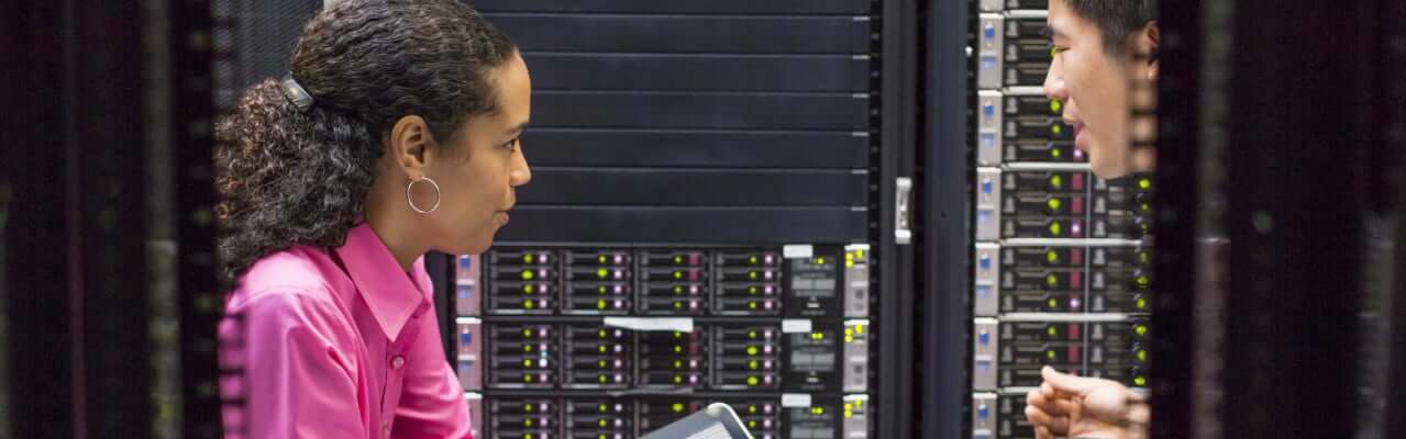 Woman with tablet and man in server room while checking servers.