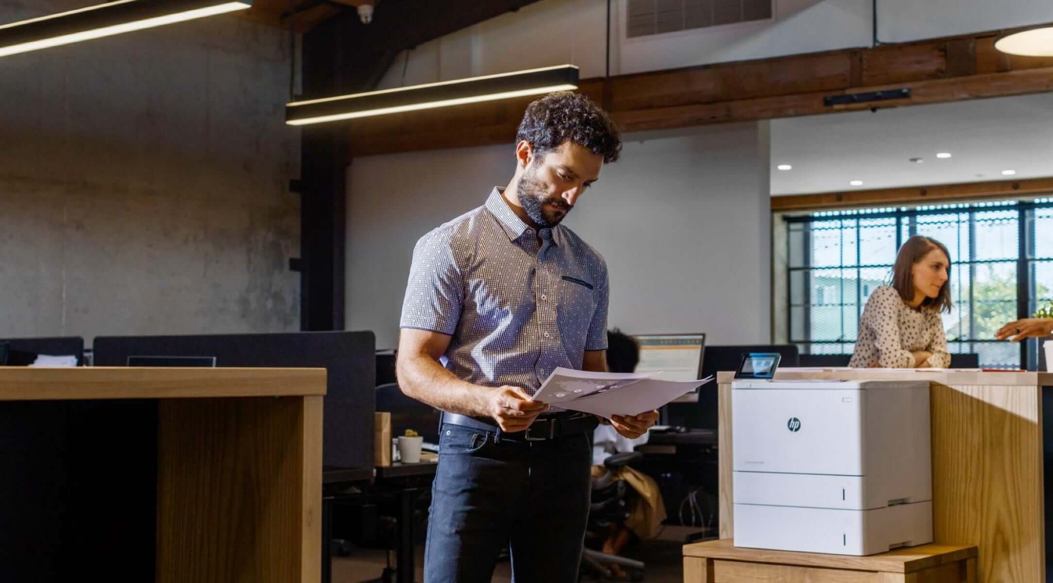 Man in casual office holding printed documents from HP LaserJet Enterprise MFP