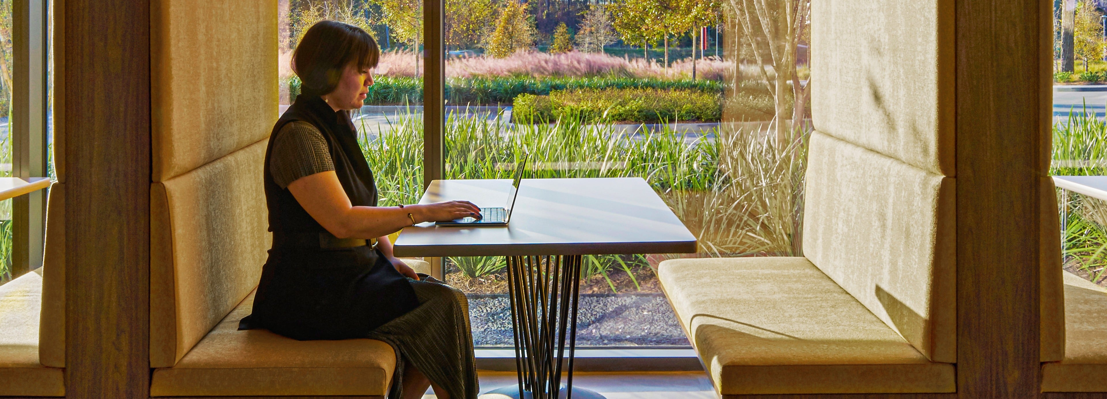 A woman sitting at a table with an HP laptop overlooking a natural landscape