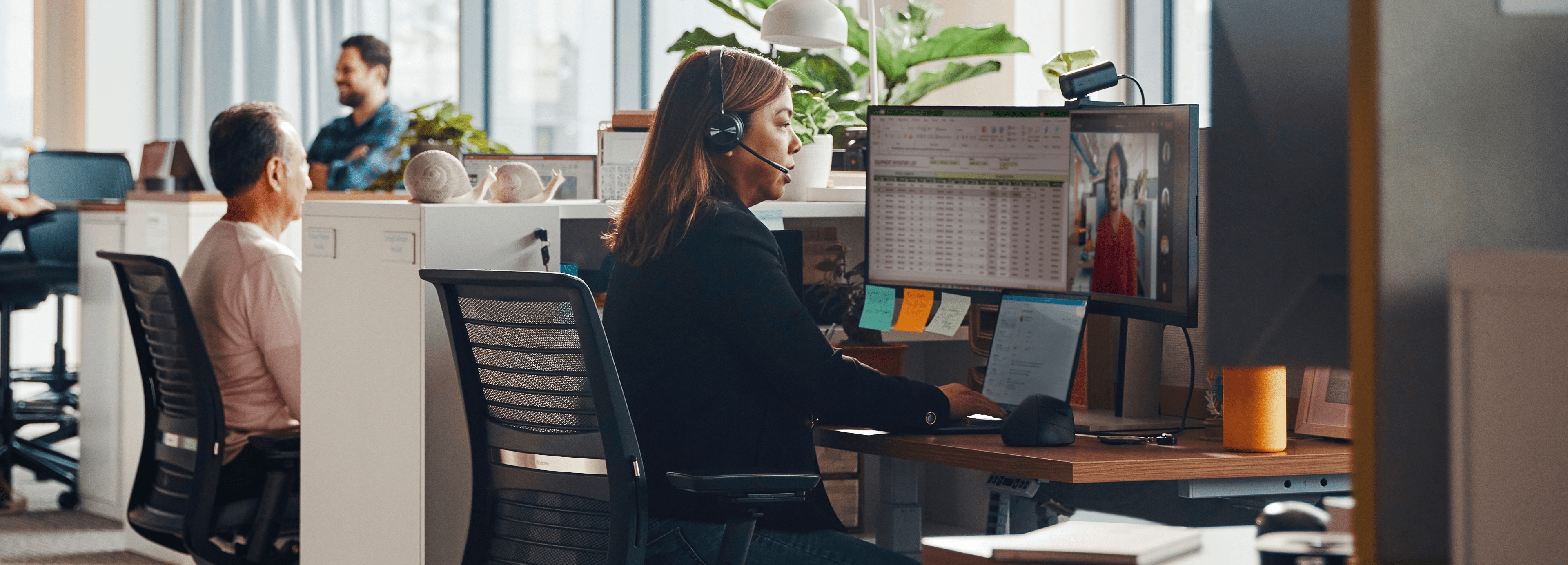 Businesswoman using a headset meeting online while sitting in front of two HP monitors.