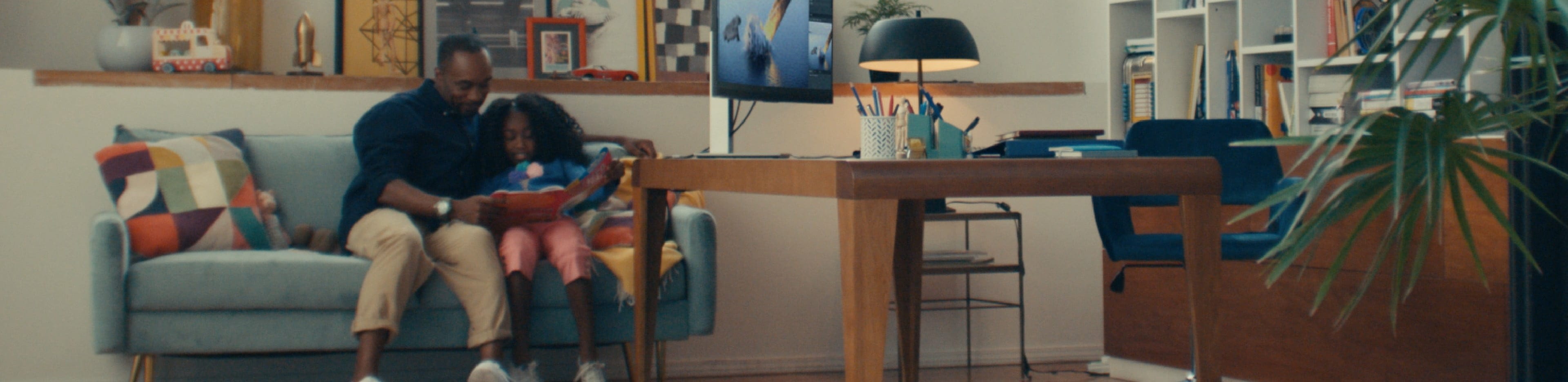 A dad and his daughter reading a book aside an HP monitor on top of a wooden desk.