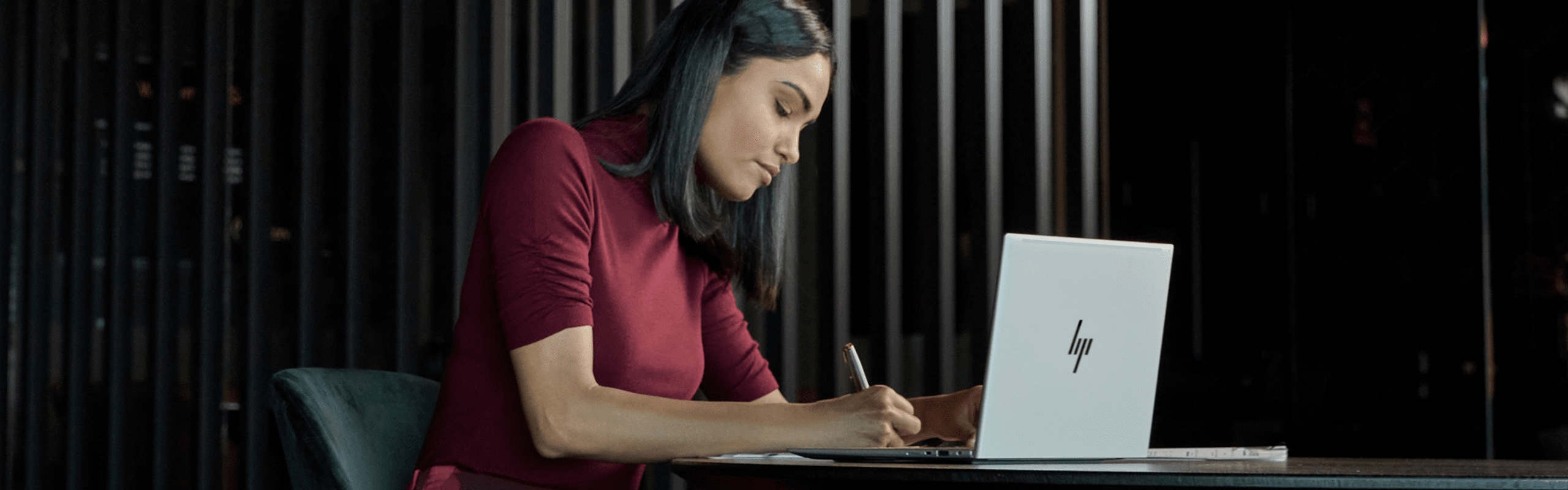 A woman taking some notes on a paper from her HP laptop.