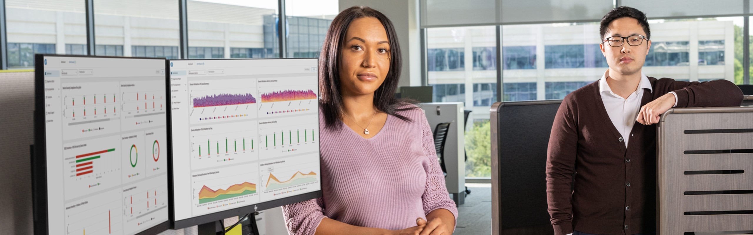 A woman and a man standing aside two HP monitors in an office desk.