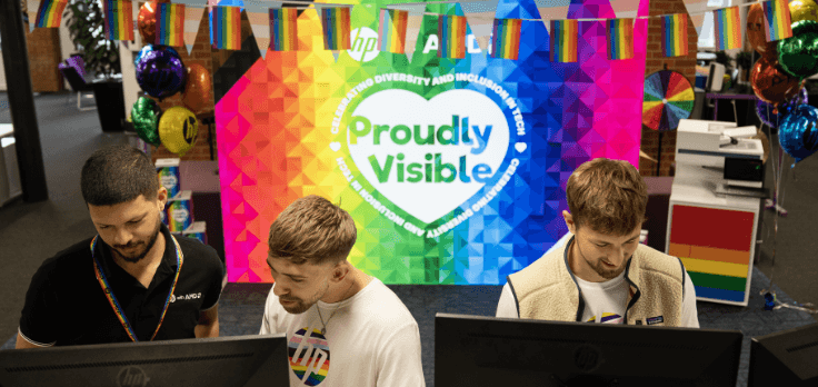 Three men working in an office with Pride decorations