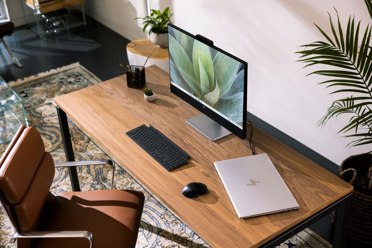 A stylish home office setup featuring a wooden desk with a large monitor, keyboard, mouse, and laptop