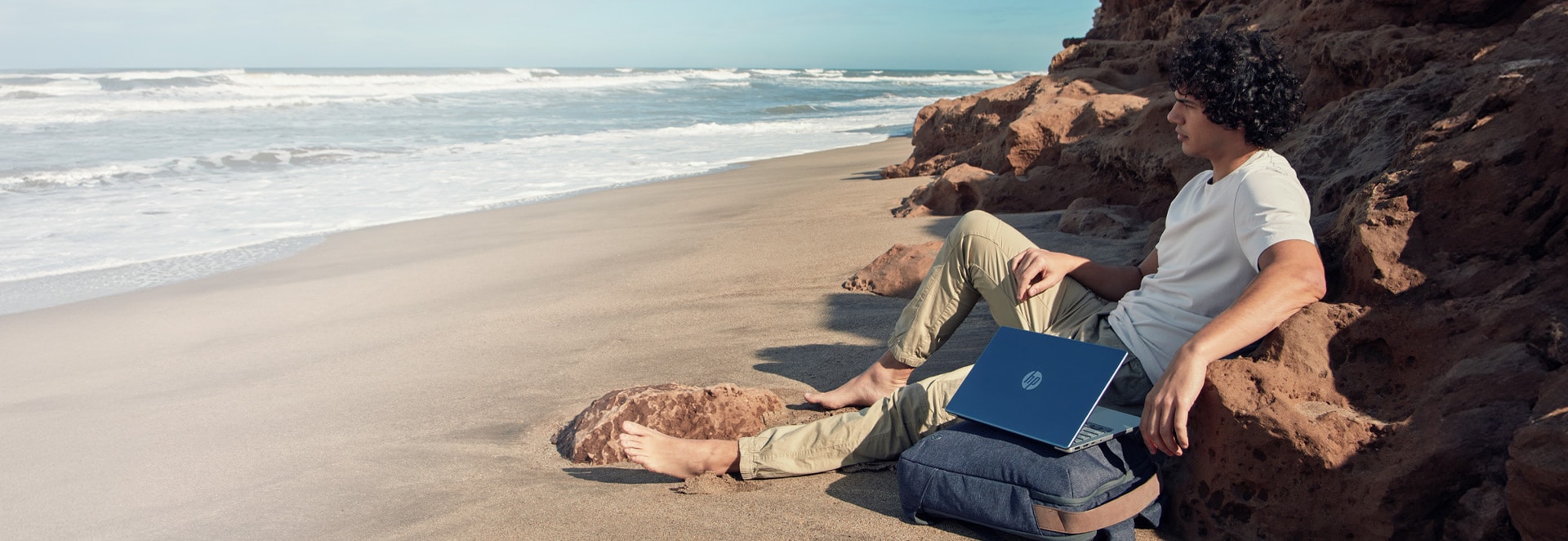 A young man sitting by the beach with his laptop 