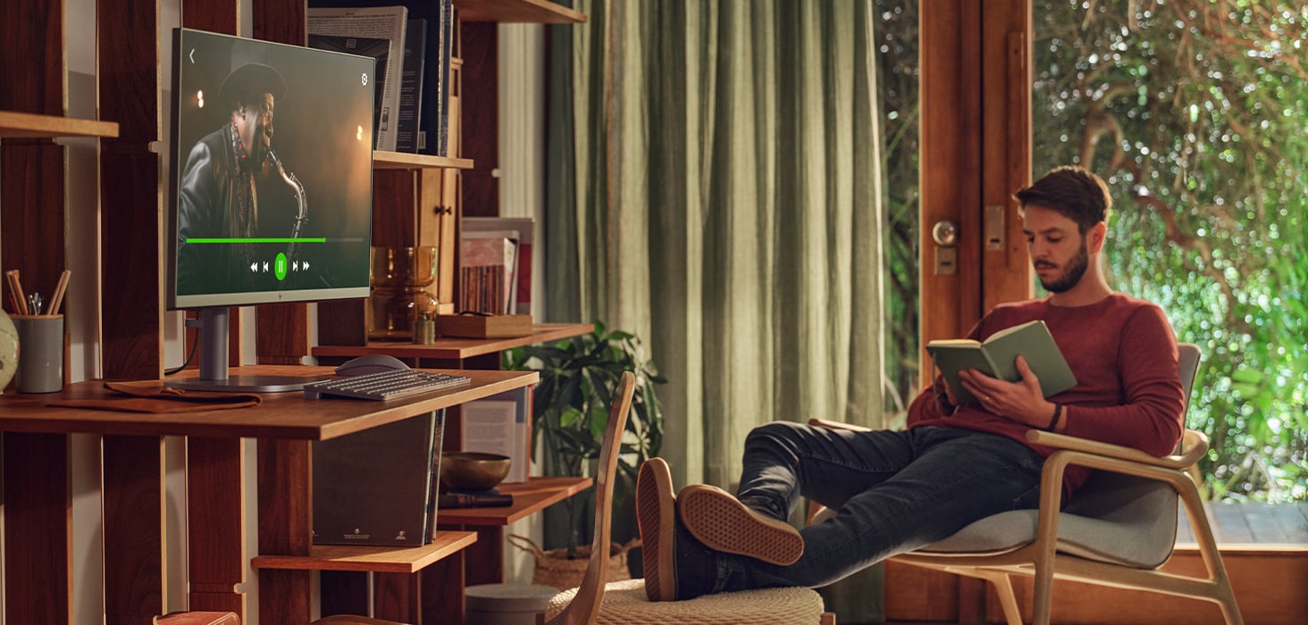 Young man reading a book while the HP OmniStudio X 27-inch All-in-One Desktop AI PC plays a music video